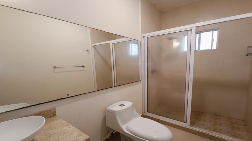 un baño con un excusado, una ducha y un espejo grande en selvanova residencial playa del carmen