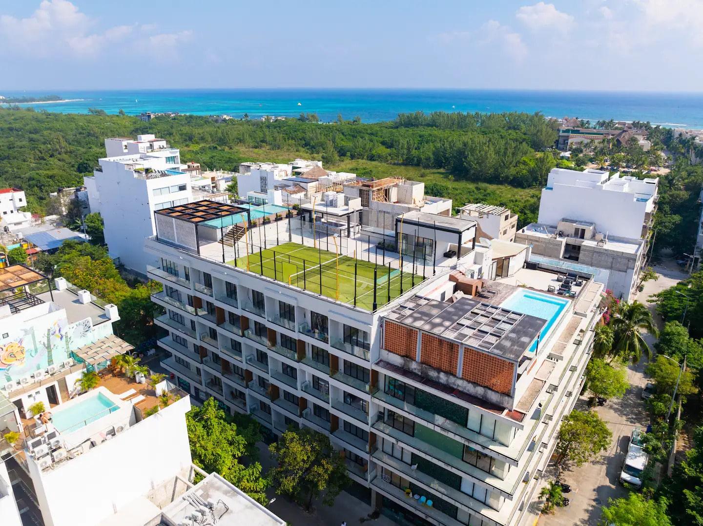 una vista aerea de un edificio con una alberca y una cancha de tenis en macondo 5ta avenida playa del carmen