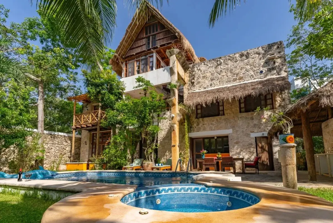 una fachada exterior de una casa grande con una alberca en el jardin en xcaret playa del carmen