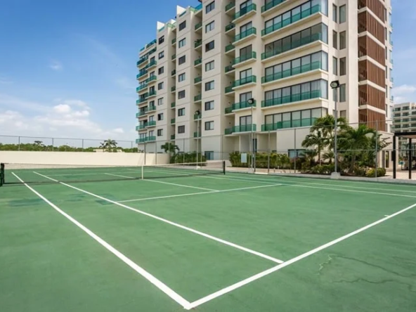 una cancha de tenis y enfrente un edificio con departamentos en venta en valle aurora playa del carmen