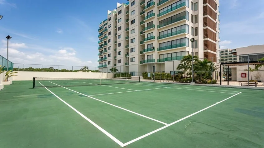 una cancha de tenis y enfrente un edificio con departamentos en venta en valle aurora playa del carmen