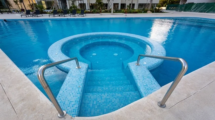 una alberca para residentes con camastros alrededor y areas verdes en valle aurora playa del carmen