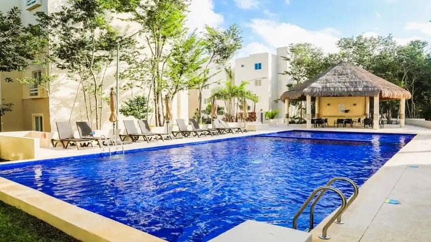 una piscina con una palapa y camastros en la selva residences playa del carmen