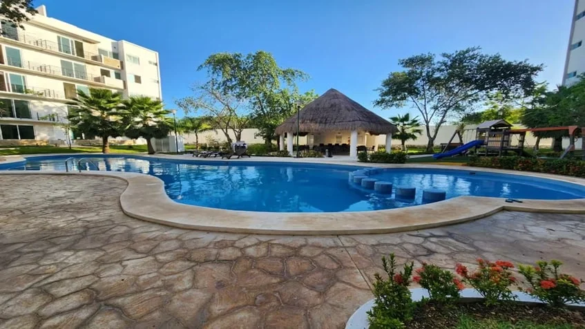 una alberca con una palapa y un edificio de departamentos en punta estrella playa del carmen