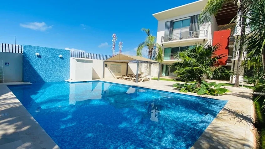 una piscina con areas verdes alrededor y camastros en edificio palmeiras playa del carmen