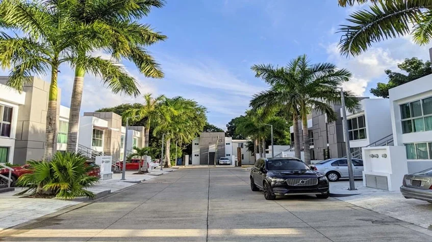 una calle con palmeras y carros estacionados en condominio anemonas playacar
