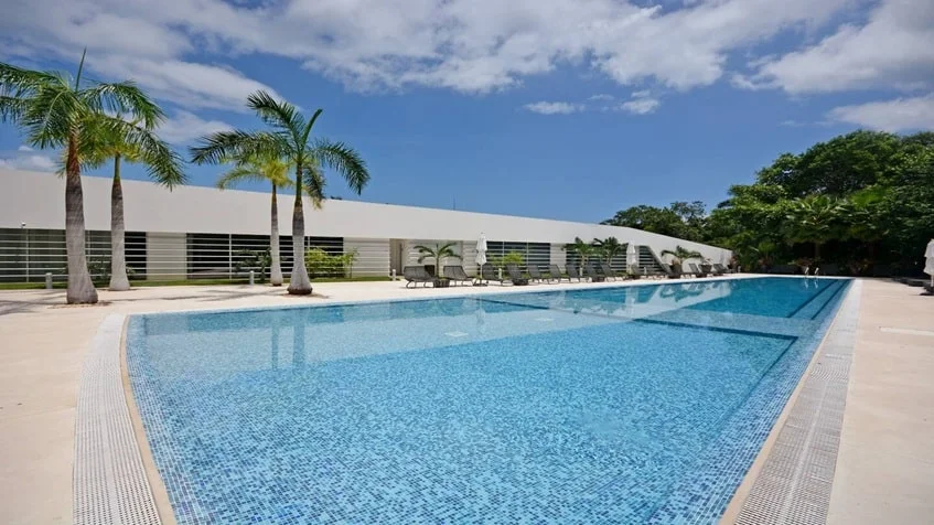 una piscina con camastros y areas verdes en lorena ochoa residences playa del carmen