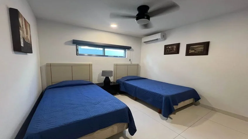 una recamara con 2 camas individuales y un ventilador y 3 cuadros decorativos en condominio anemonas playacar