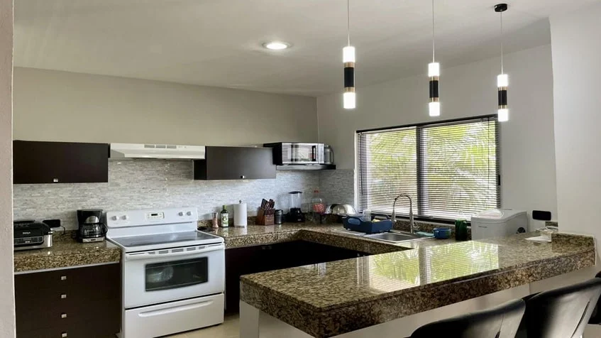 una cocina con una estufa electrica y barra de granito en condominio alegro playa del carmen