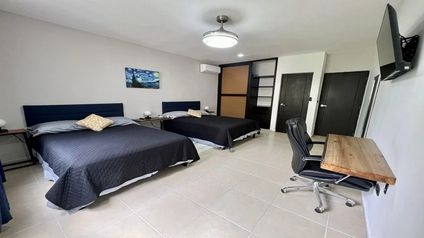 una recamara principal con 2 camas, un escritorio de trabajo y una tv en condominio alegro playa del carmen