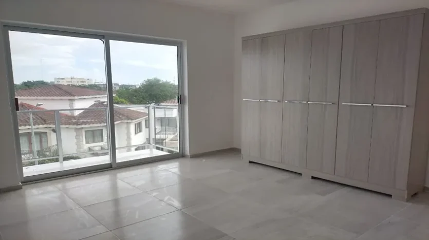 una recamara secundaria con vista al exterior y un balcon en condo jim ejidal playa del carmen